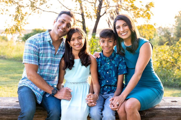 Family photos at sunset, Winfrey Point, White Rock Lake - A joyful family of four hugging tightly with a golden fall sunset glowing in the background.